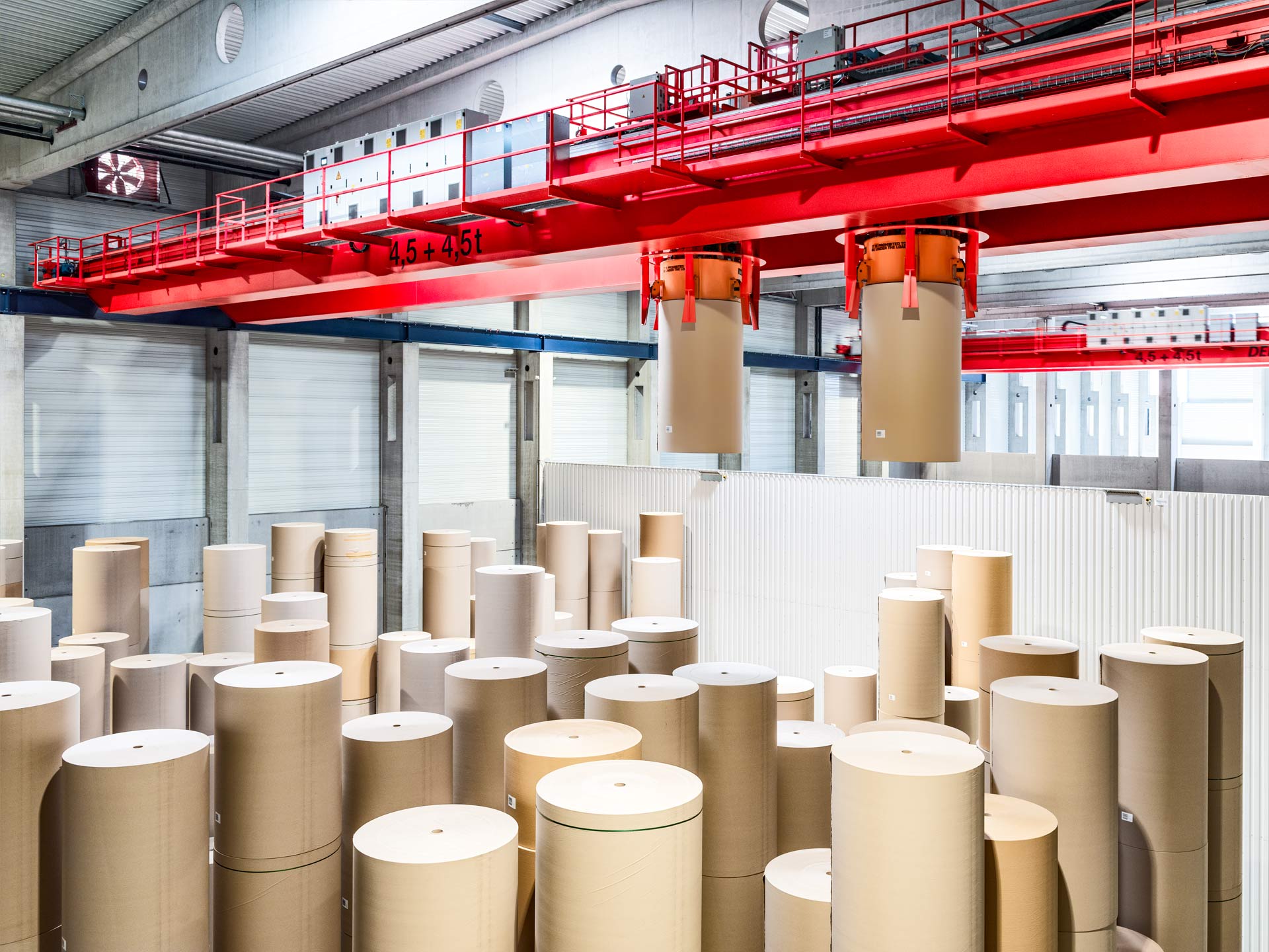 Eine Lagerhalle mit Papierrollen, die mithilfe zweier Greifarme von einem Prozesskran transportiert werden.